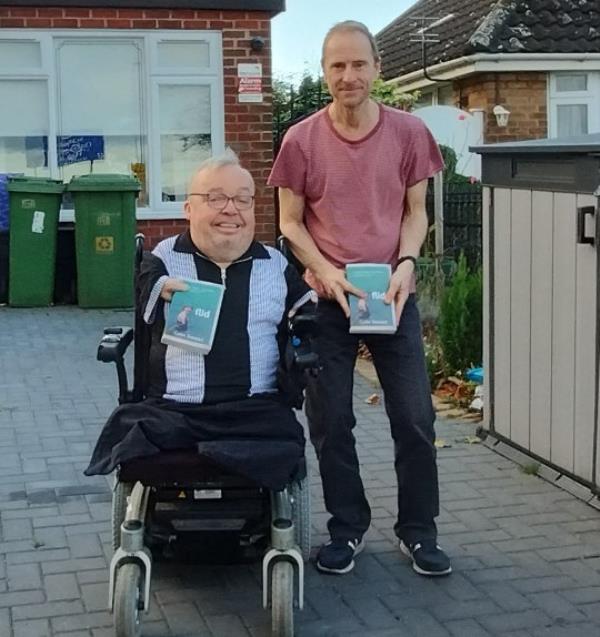 Kevin Do<em></em>nnellon and Colin Stewart side by side in front of a house. Both are holding copies of Flid by Colin Stewart.