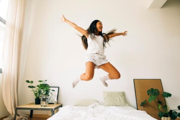 Exuberant young woman jumping on bed