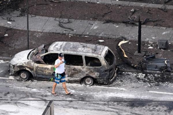 An aerial image taken on August 10, 2023 shows a person walking past a destroyed car in the aftermath of wildfires in western Maui in Lahaina, Hawaii. At least 36 people have died after a fast-moving wildfire turned Lahaina to ashes, officials said August 9, 2023 as visitors asked to leave the island of Maui found themselves stranded at the airport. The fires began burning early August 8, scorching thousands of acres and putting homes, businesses and 35,000 lives at risk on Maui, the Hawaii Emergency Management Agency said in a statement. (Photo by Patrick T. Fallon / AFP) (Photo by PATRICK T. FALLON/AFP via Getty Images)